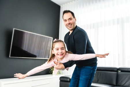 Dad with his cute little girl on a modern house having fun doing air plane on the living roomの写真素材