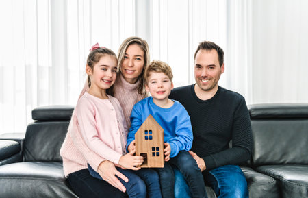 Family of four having fun on new modern house holding wood houseの写真素材