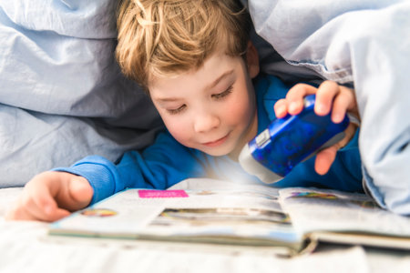 Little boy lying on bed reading book at homeの写真素材
