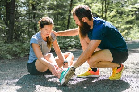 woman having ankle injury with men trying to helpの写真素材