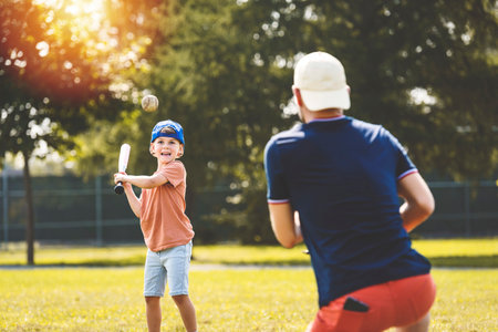 Father and son playing baseball in sunny day at public park