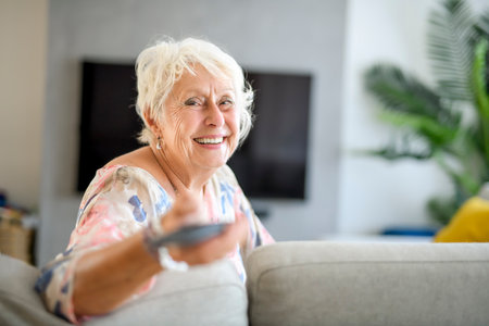 Active beautiful senior woman in the living room with remote control