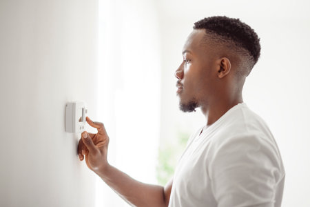 A Smiling Man Adjusting Thermostat On Home Heating Systemの写真素材