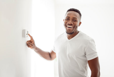 A Smiling Man Adjusting Thermostat On Home Heating Systemの写真素材