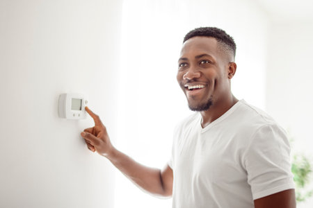 A Smiling black Man Adjusting Thermostat On Home Heating Systemの写真素材