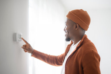 A Smiling black Man Adjusting Thermostat On Home Heating System