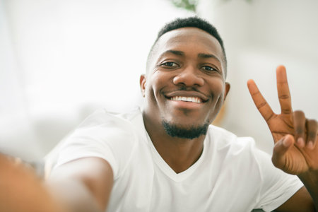 Black men wearing white shirt in studio shot on white background holding cellphone and take selfieの写真素材