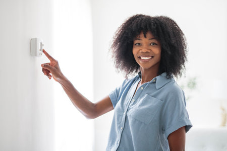 black woman lady adjusting the climate control panel on the wall wall thermostatの写真素材