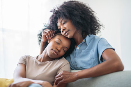 Affectionate mother and daughter sitting on sofa at homeの写真素材