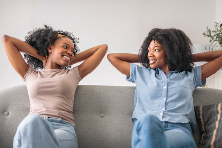 Affectionate mother and daughter sitting on sofa at homeの写真素材