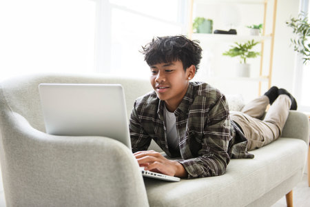 thai teen using laptop at home sofa