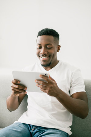 Black men wearing white shirt on sofa holding tabletの写真素材