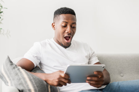 Black men wearing white shirt on sofa holding tabletの写真素材