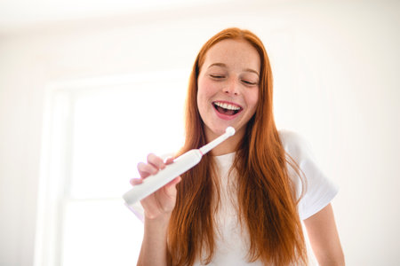 A cheerful woman happily enjoys her morning routine while brushing her teeth in a bright, sunny bathroomの写真素材