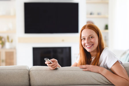Beautiful young woman holding tv remote control and changing TV channels