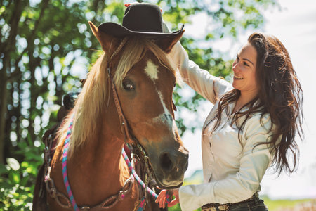 woman cowgirl, stands next to her horse in summer seasonの写真素材