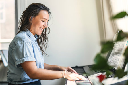 happy woman playing piano inside house on the living roomの写真素材