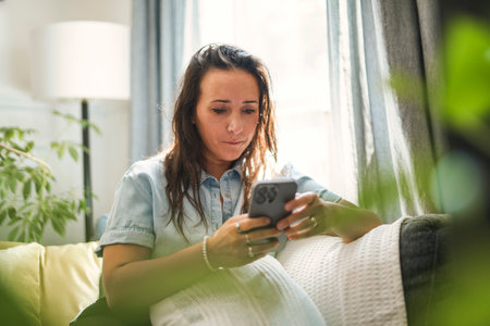 Beautiful 40s woman on the living room interior using cellphoneの写真素材