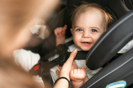 Portrait of adorable infant baby girl which unrecognizable young mother fastening safety belt in car seat.の写真素材