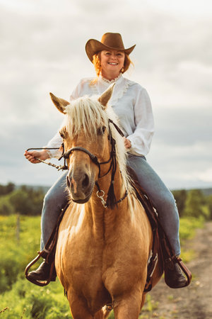 A woman, wearing a cowboy hat, is riding her horse down a dirt roadの写真素材