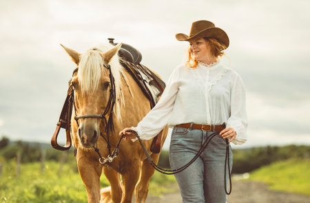 A woman, proudly wearing a cowboy hat, stands next to her horseの写真素材