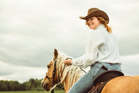 A woman is wearing a cowboy hat while riding a horse in an open field