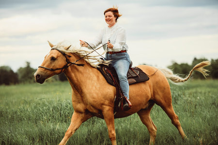 A woman is skillfully riding a horse gracefully in a lush fieldの写真素材