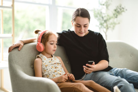 babysitter teen sit on sofa listening music with cute 5 years child girl