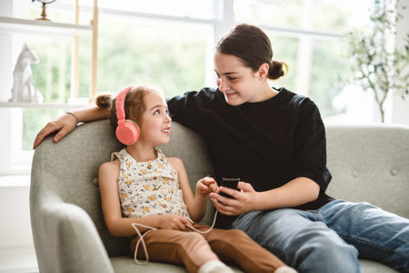 babysitter teen sit on sofa listening music with cute 5 years child girl