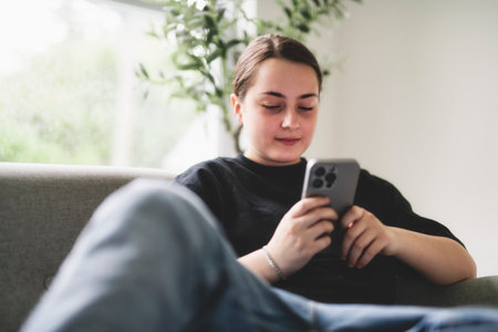 15 years old girl sit on sofa at home with cellphoneの写真素材