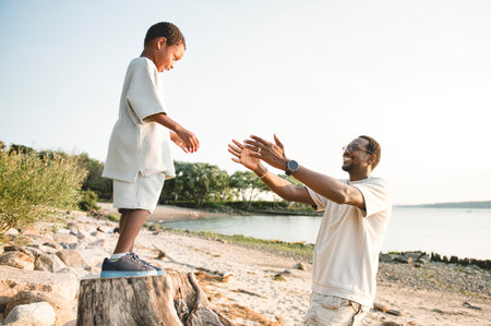 Cheerful black american father and is son against beautiful seascapeの写真素材