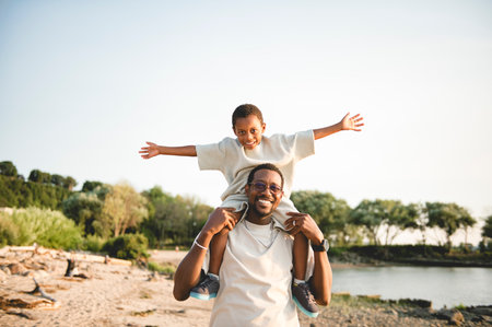 Cheerful black american father and is son against beautiful seascapeの写真素材