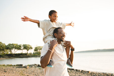 Cheerful black american father and is son against beautiful seascapeの写真素材