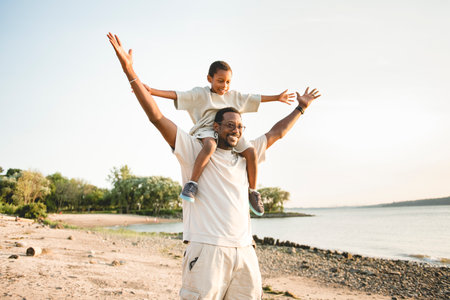 Cheerful black american father and is son against beautiful seascapeの写真素材