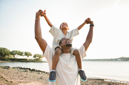 Cheerful black american father and is son against beautiful seascapeの写真素材