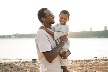 Cheerful black american father and is son against beautiful seascapeの写真素材