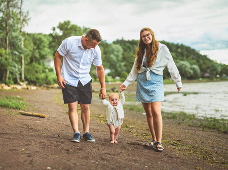 family with baby child girl at the sunset on the waterscape view from backの写真素材