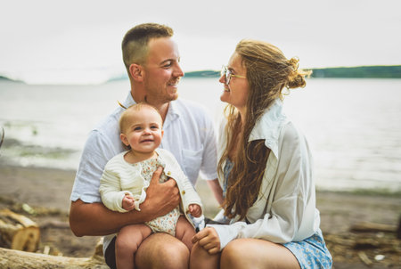 family with baby child girl at the sunset on the waterscape view from backの写真素材