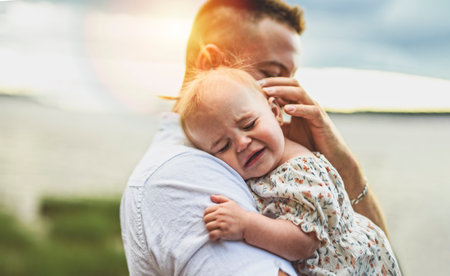 father and baby child girl consoling at the sunset on the waterscape view from back