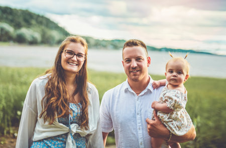 family with baby child girl at the sunset on the waterscape view from back