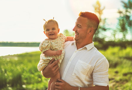 father and baby child girl at the sunset on the waterscape view from backの写真素材