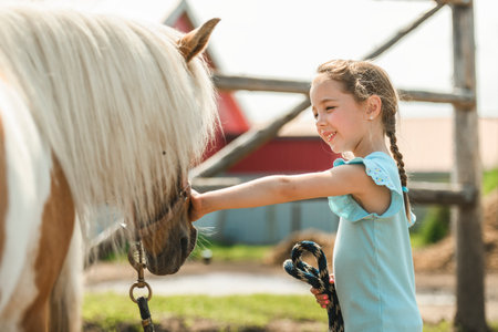 Cute little girl petting a pony in a farmの写真素材