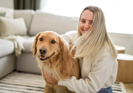 Portrait of a young woman on the livingroom with golden retriever dog indoors at home.の写真素材