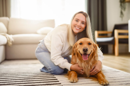 Portrait of a young woman on the livingroom with golden retriever dog indoors at home.の写真素材