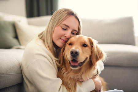 Portrait of a young woman on the livingroom with golden retriever dog indoors at home.の写真素材