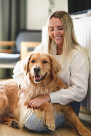 Portrait of a young woman on the livingroom with golden retriever dog indoors at home.の写真素材