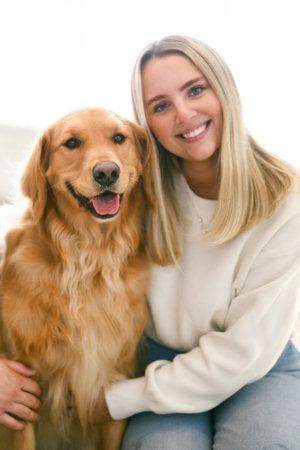 Portrait of a young woman on the livingroom with golden retriever dog indoors at home.の写真素材