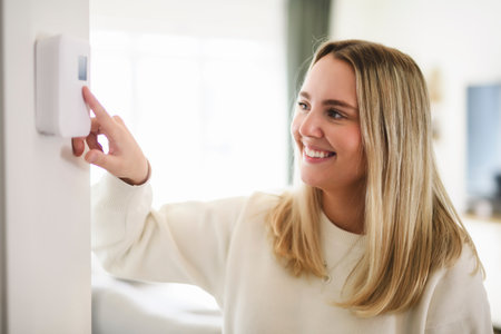 Smiling woman using modern smart home system, controller on wall