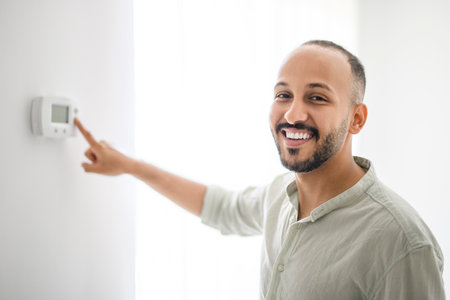 Hispanic Man adjusting room temperature with electronic thermostat at homeの写真素材