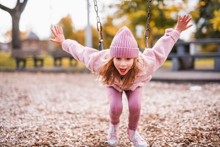 Little girl having fun on a playground in public park on autumn day.の写真素材